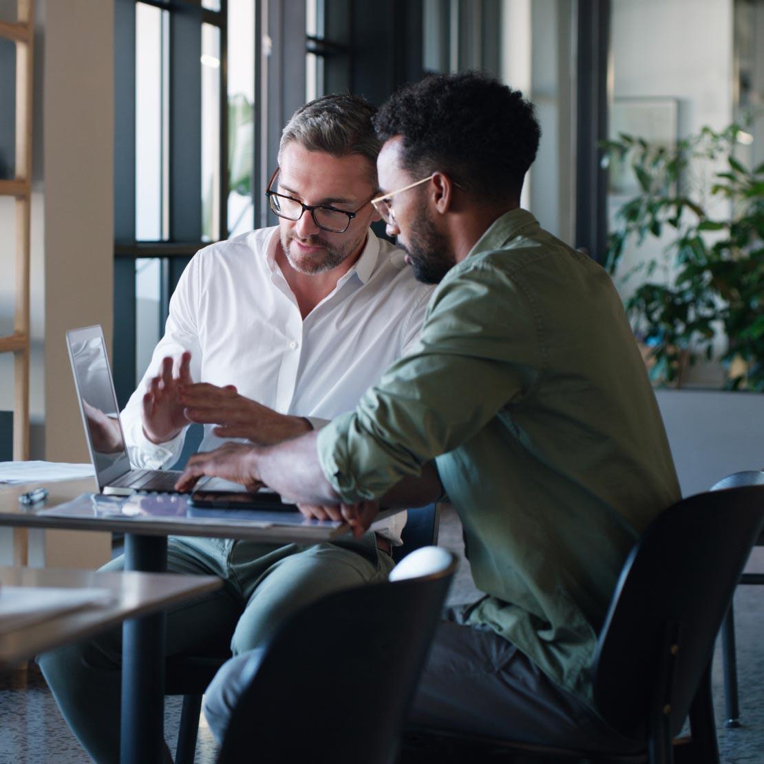 Two men at a table with laptops, discussing risk management challenges due to siloed products and lack of context.Two men at a table with laptops, discussing risk management challenges due to siloed products and lack of context.