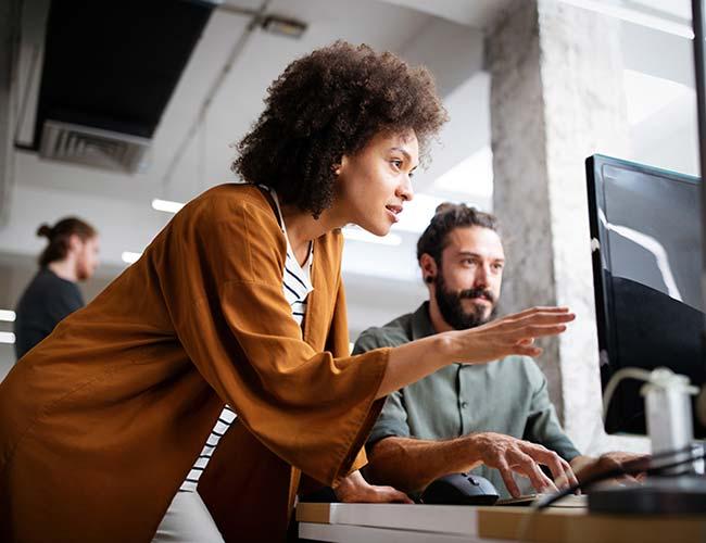 A woman and man collaborate on a computer in an office, exploring online courses and training opportunities.