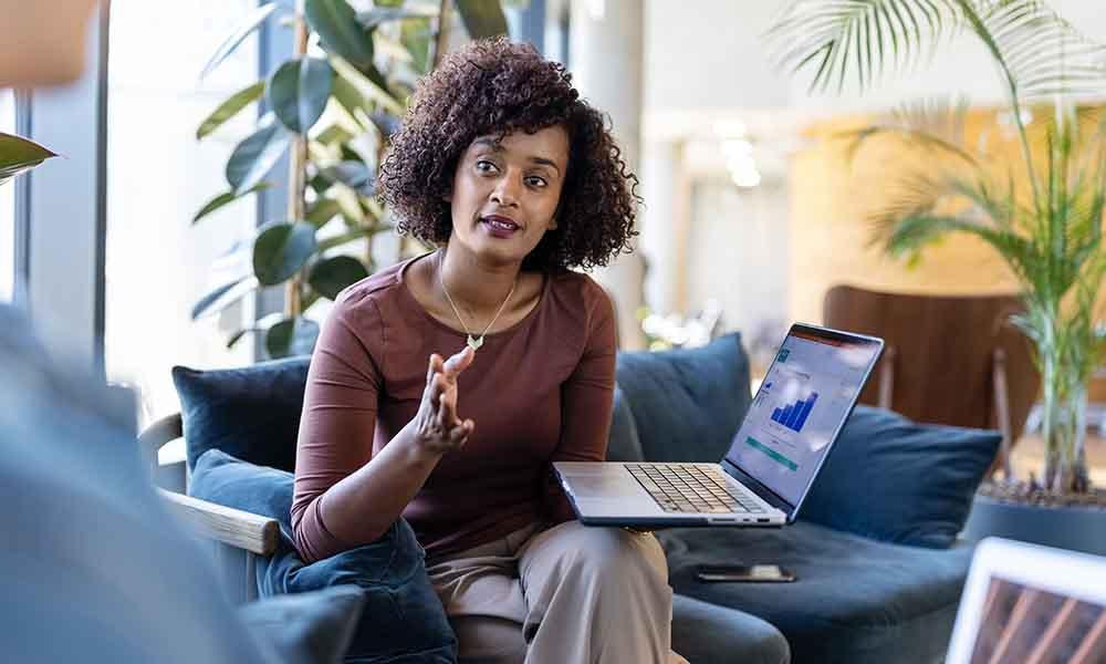 In an office, one woman speaks to another, highlighting dynamic dashboards and reports for security and performance metrics.