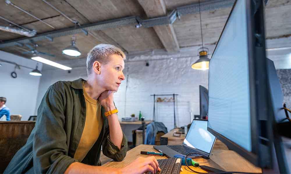 A woman diligently works on a computer in an office, managing her tasks and assessing risk exposures effectively.