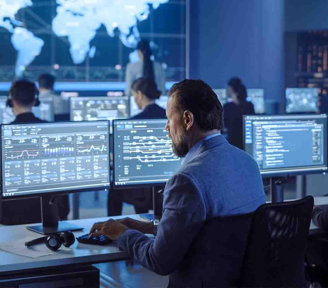 A suited man at a desk with several monitors, engaged in risk management and vulnerability assessment tasks.
