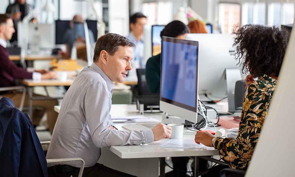 A man and woman seated at a desk in an office, engaged in discussions about automated ticket assignment and risk management.