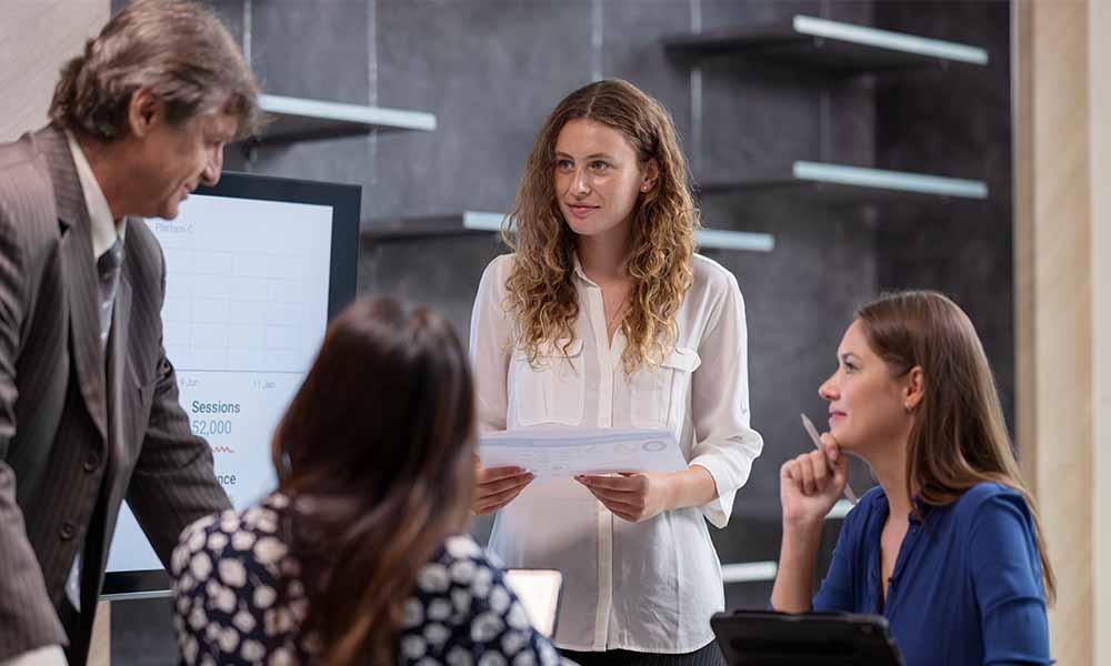 A woman addresses a group in an office setting, discussing strategies for integrating vulnerability data and risk management.